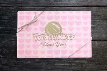 light pink box with darker pink hearts wrapped in a gold ribbon with gold Totally Nuz logo which reads: Totally Nutz about you!